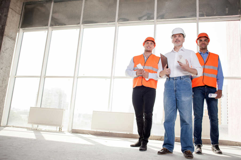 Experienced old architect and two workers are standing and waiting for a customer. They are holding a folder of document and blueprints. The men are smiling. Copy space in left side